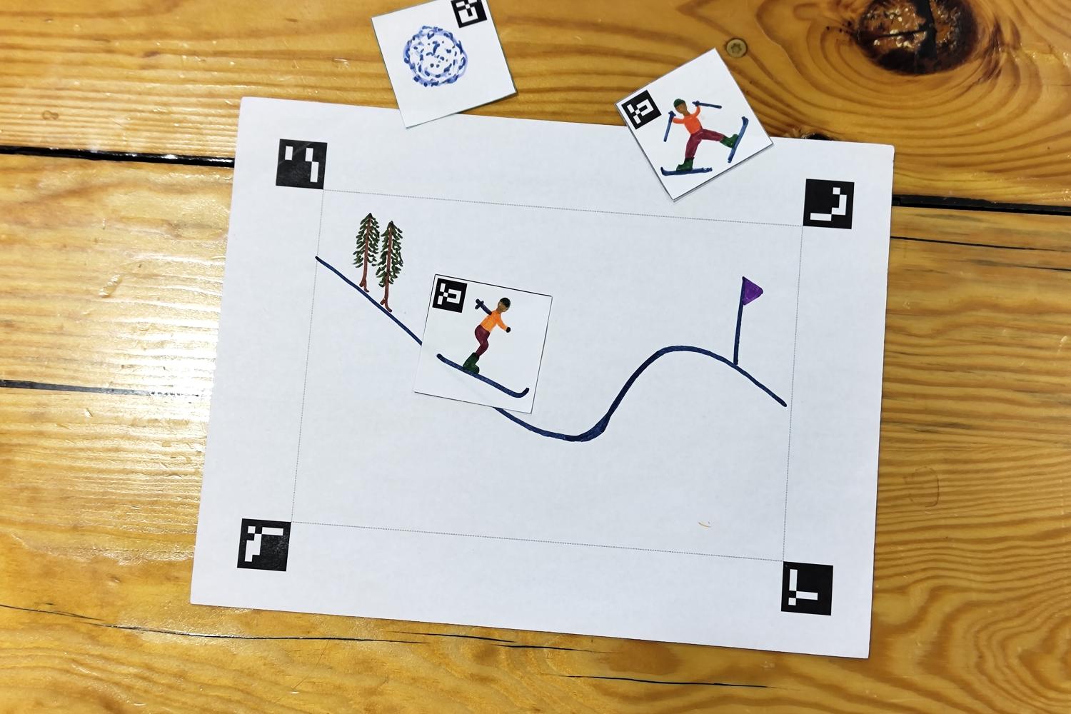 Cartoon drawing of a skiing scene on paper, small paper cutouts have drawings of people skiing