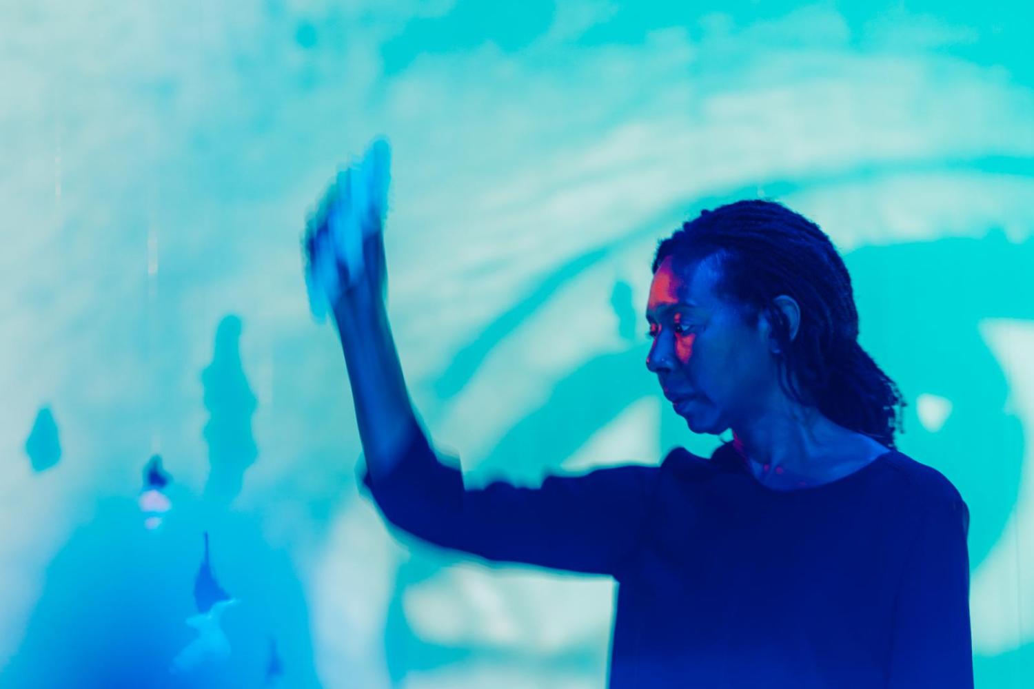 artist holding a sculpture in a blue projected landscape