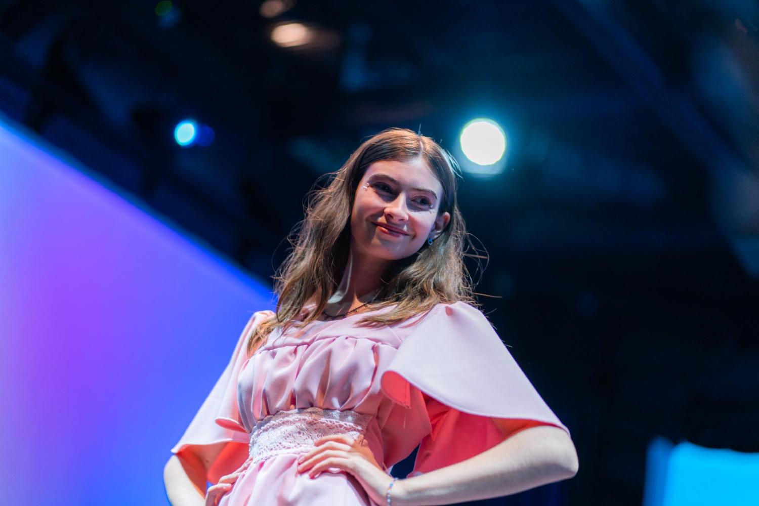 teen model posing in a pink dress with a stage light lighting them from the back