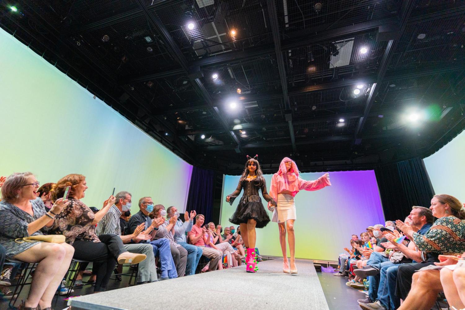 two teen models walking the runway hand in hand one with a goth black outfit the other with a pink one