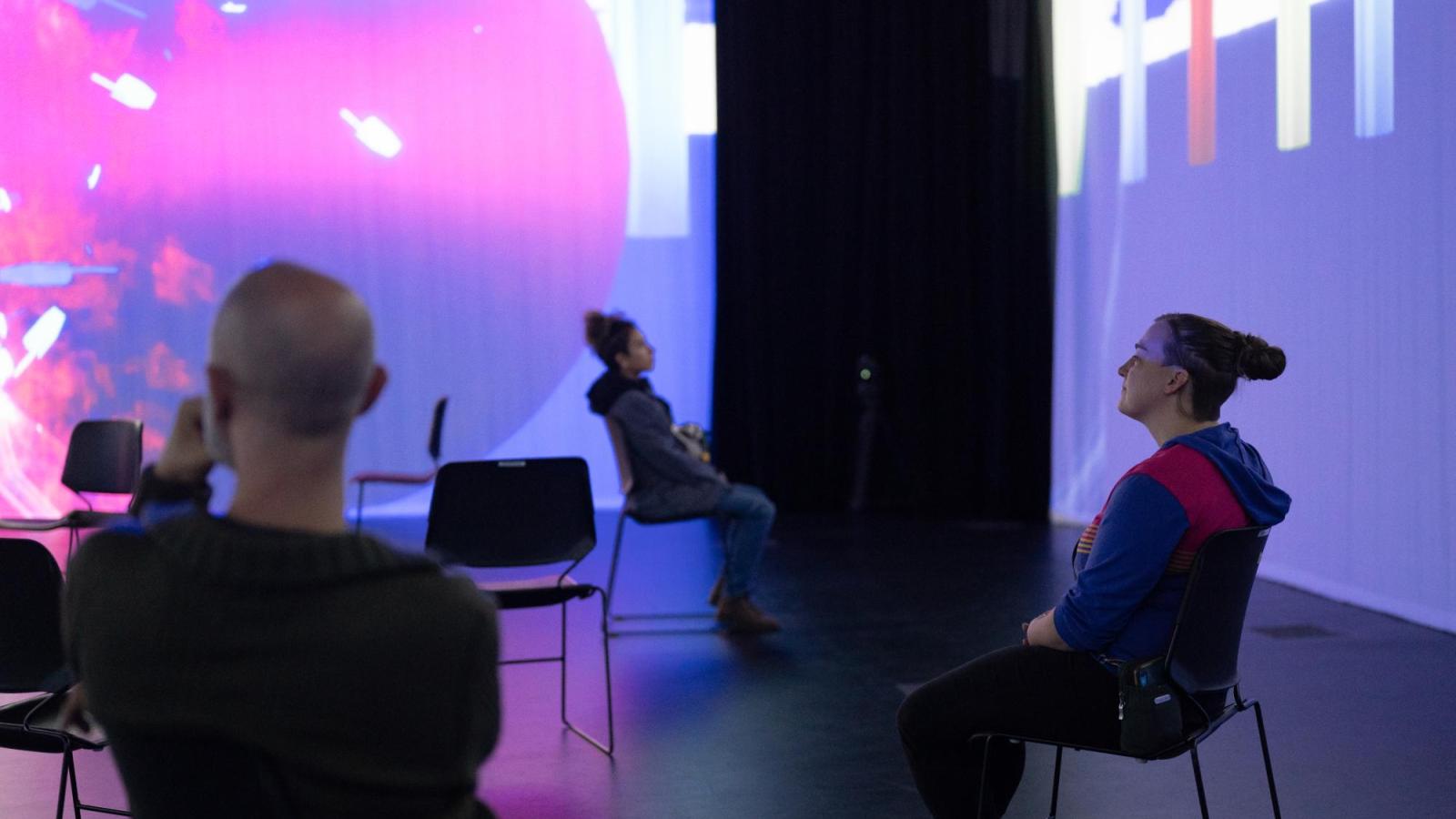 people sitting in a room filled with purple and pink projections