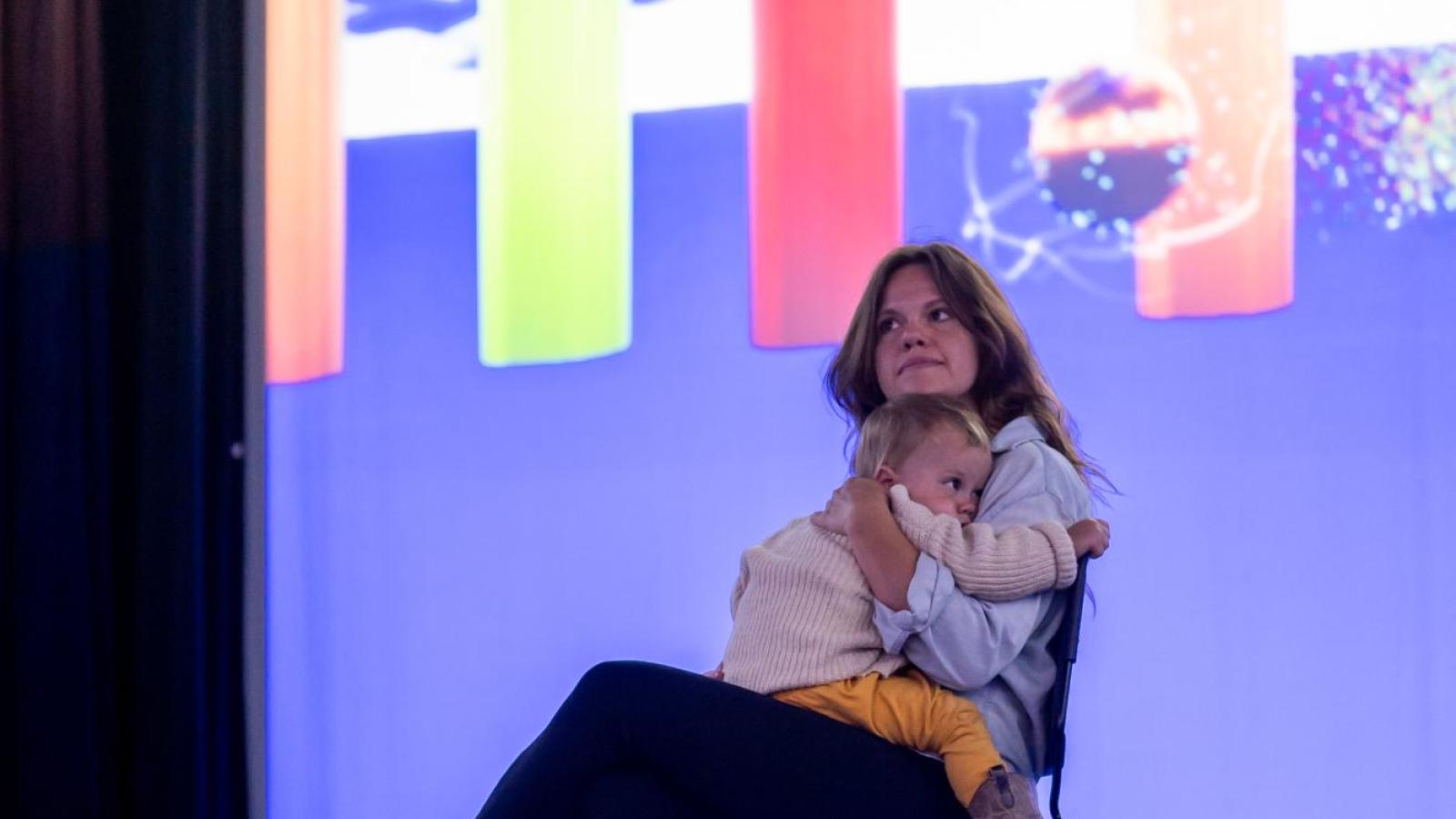 person cradling a child while looking around at the colorful projections