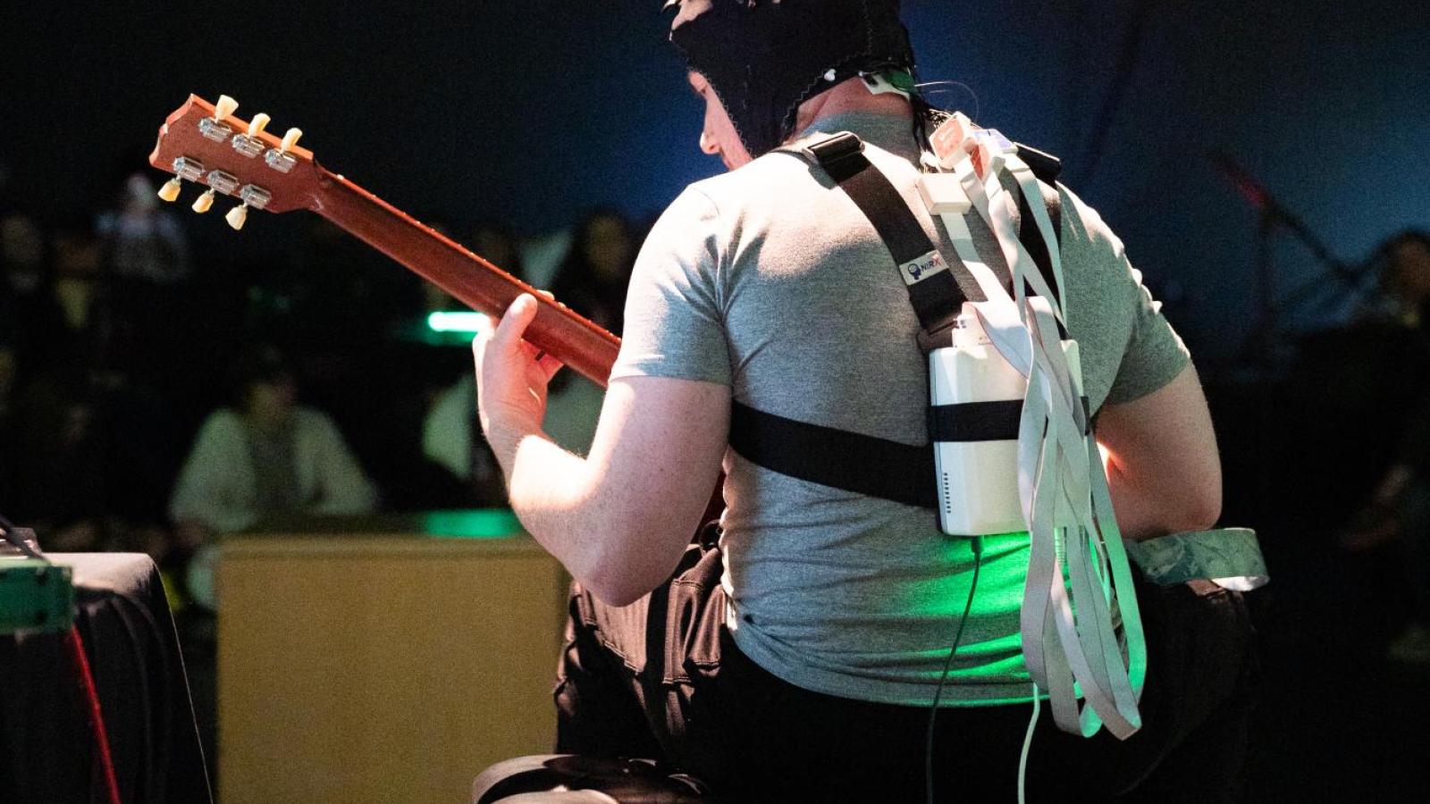 backlit shot of guitar performer playing while hooked up to brain scanner