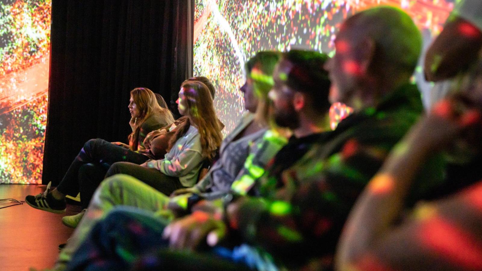 audience looking on in a colorfully lit room