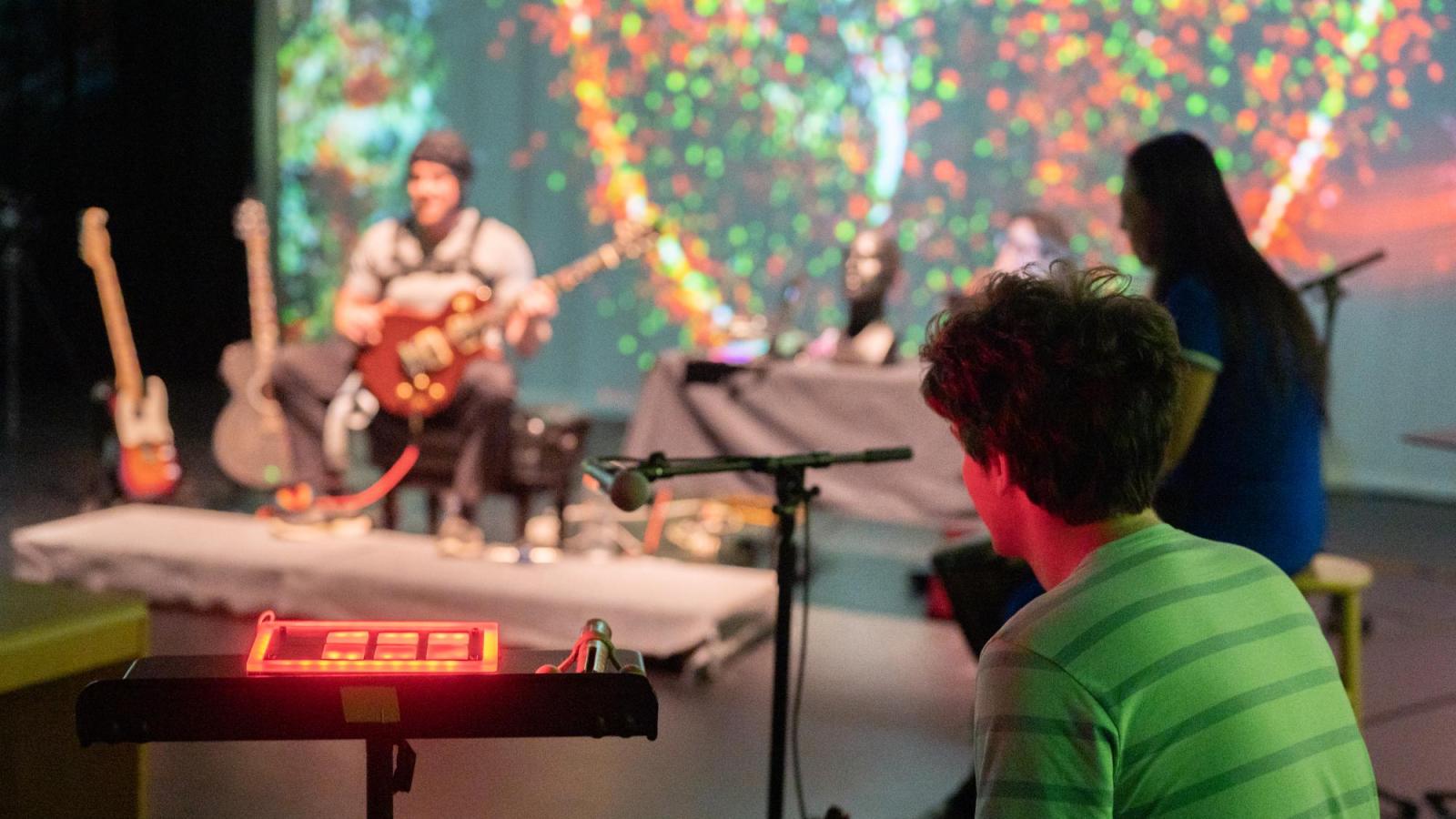 someone looks on with a red control panel in front of them while guitar performer plays