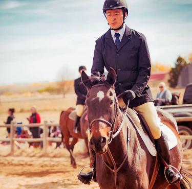 Weiliang “Albert” Jin with a helmet on riding a horse.