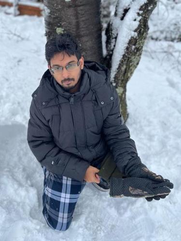 Aseem Visal kneels in the snow by a tree