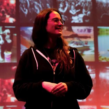 Monica Bolles speaking in front of a screen projecting many images under dramatic lighting