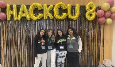 Hack CU winners stand on stage below balloons spelling "HackCU."