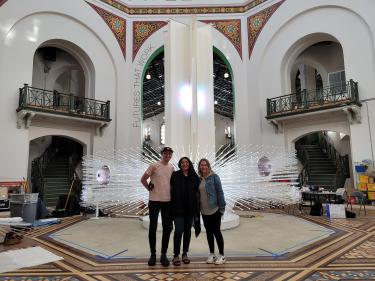Justin Gitlin stands in front of the "Me + You sculpture at the Smithsonian with Suchi Reddy and an unidentified person.