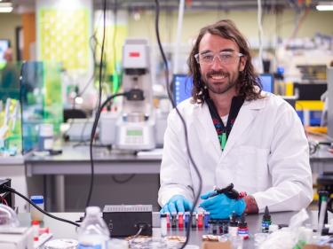 Carson Bruns in a white lab coat working with tattoo equipment in his lab