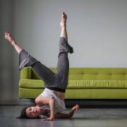 dancer ondine geary on concrete floor with shoulder and head on ground and feet in air with green sofa behind