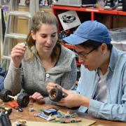 Two students smile as they build a remote control car from cardboard, salvaged parts and micro:bits