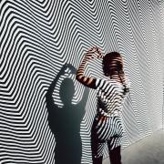 Woman stands in front of a black and white striped wall in the Moire Room at Meow Wolf Denver.