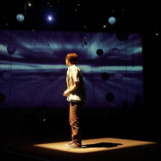 From a past show in the black box a person looks to a background that looks like planets.