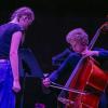 An artist bows a double bass while another artist looks on
