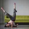 dancer ondine geary on concrete floor with shoulder and head on ground and feet in air with green sofa behind