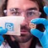 Carson Bruns, holds his gloved hands forward and holds a wooden CU logo in his left hand and a piece of pig's skin with the CU logo on it outlined by a square of blue ink
