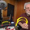 Wayne Seltzer holds several face shield parts next to his 3D printer, which is making several more.