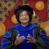 Donna Auguste giving a virtual commencement speech, dressed in graduation regalia.