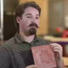 Christopher Gaines holds clay-colored square with a tactile representation of a sun petroglyph