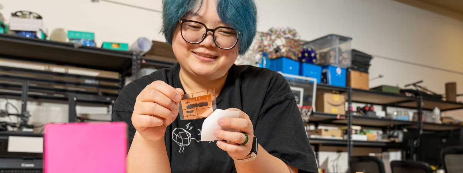 An asian woman with but hair and glasses holding a transparent circuit board.