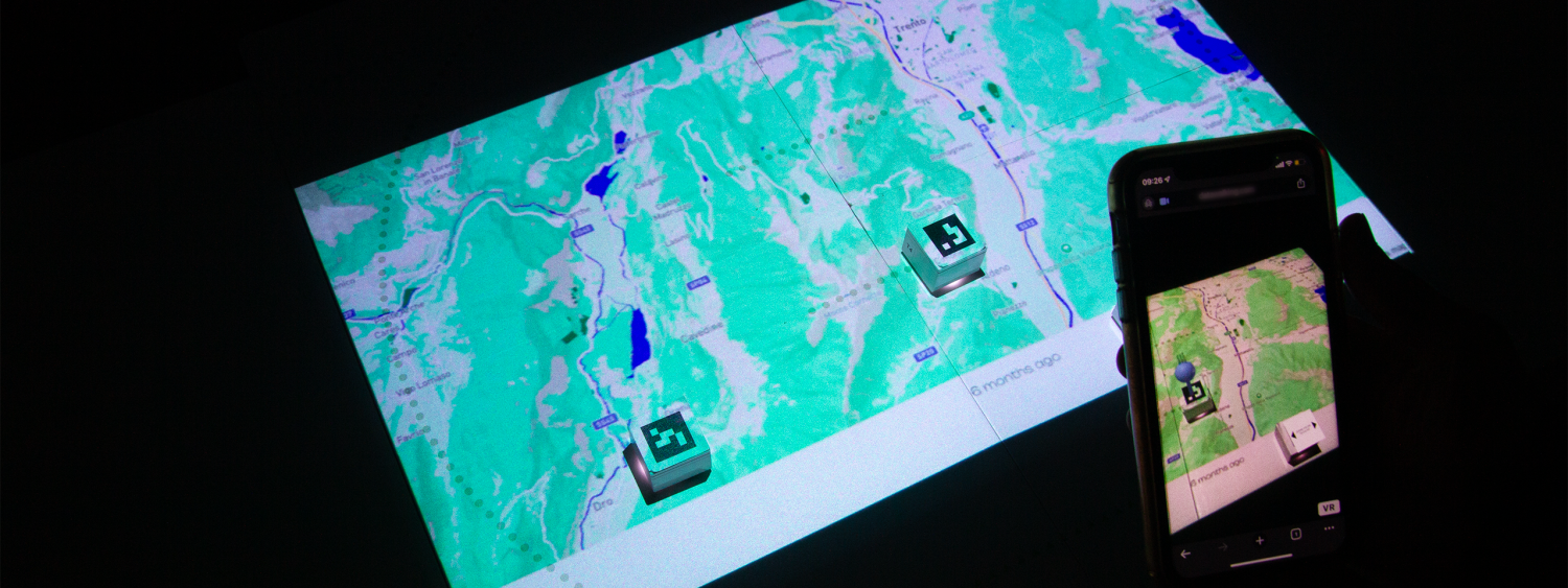 A map projected onto a surface. Two paper blocks are on the map, which show as pins through a phone screen.