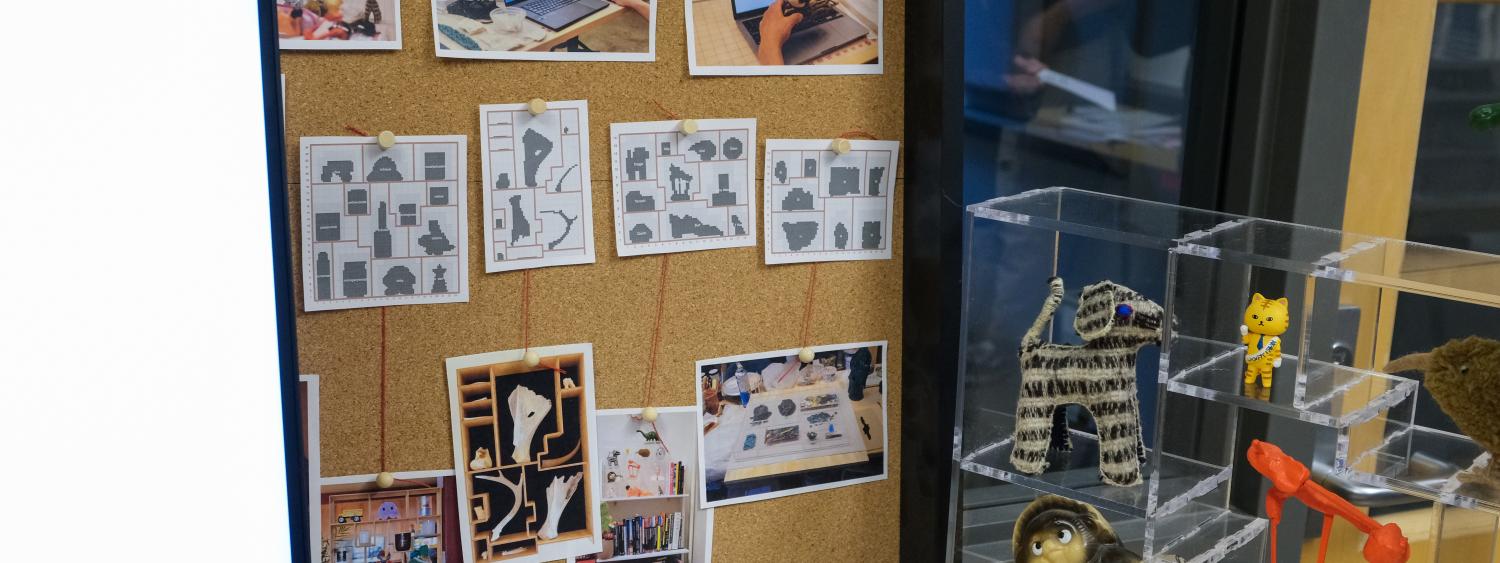 A corkboard displays various knolling pattern. A small clear display shelf is to the right containing various small figurines.