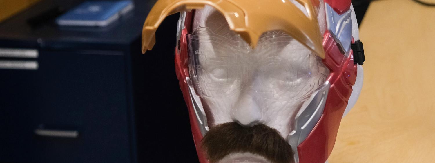 A mannequin head with a fake mustache wearing an open Ironman mask.