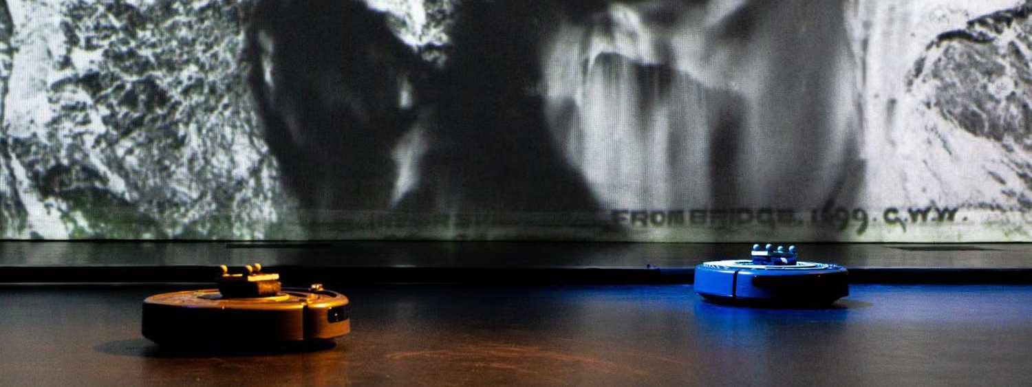 A dark room with white abstract textures projected onto the wall. Two discs lit in orange and blue are on the floor.