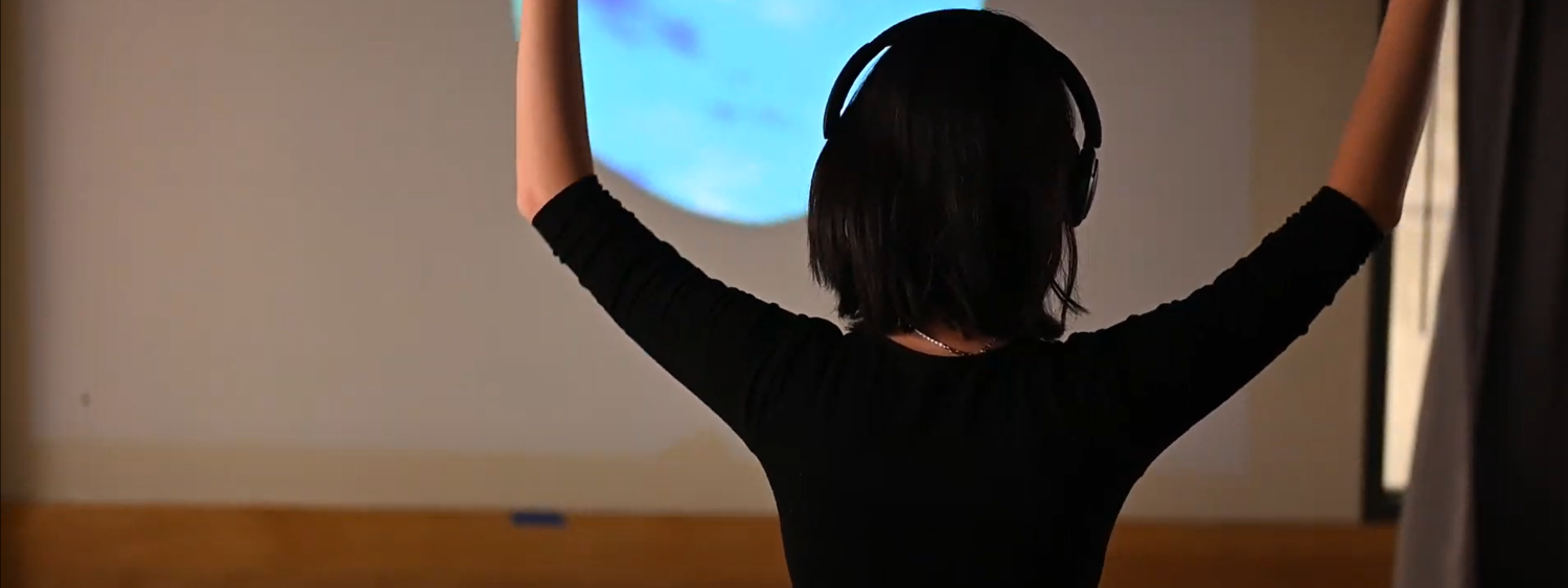 A person with headphones is raising their hands above their head. In front of them is a blue moon projected on the wall.