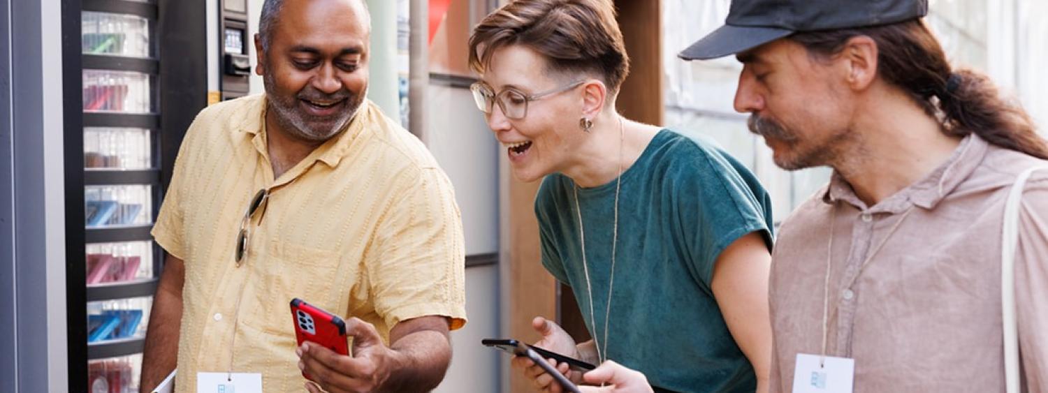 Three people looking down at their phones, smiling