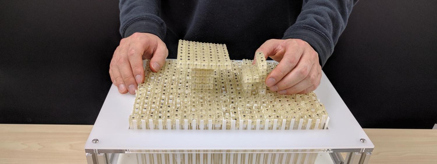 Dynablock constructs a miniature 3D model by assembling 3,000 9 mm blocks, leveraging a 24 x 16 pin-based shape display as a parallel assembler.