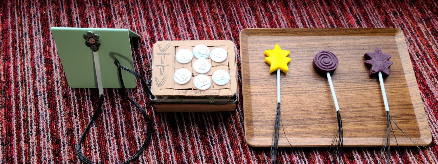 Vibrotactile tongue vision system, also known as VT-TV. A seven-segment vibration motor lollipop connected to a controller with seven pressure sensors. Three examples of the vibration motor lollipop encased in different shaped gummy candy.