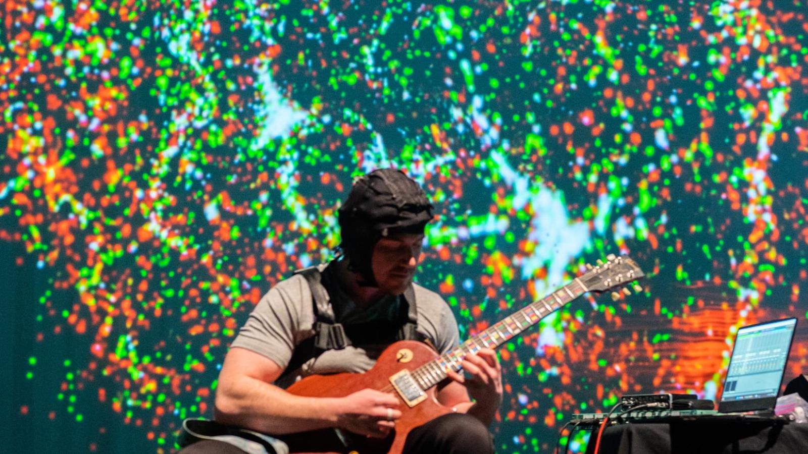 projection of exploding colors in the background while man performs guitar