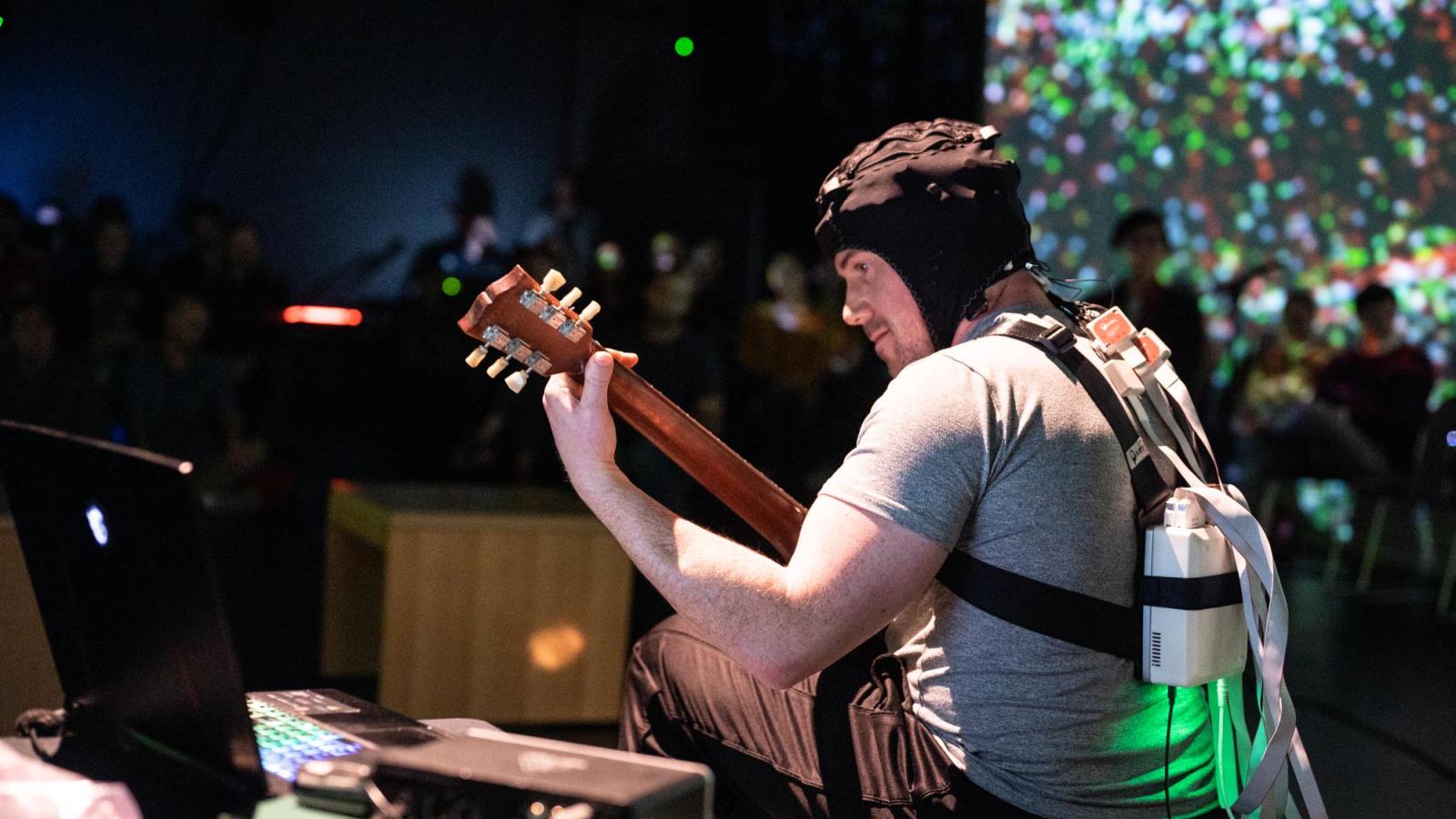 man in playing guitar while wearing a brain scanner