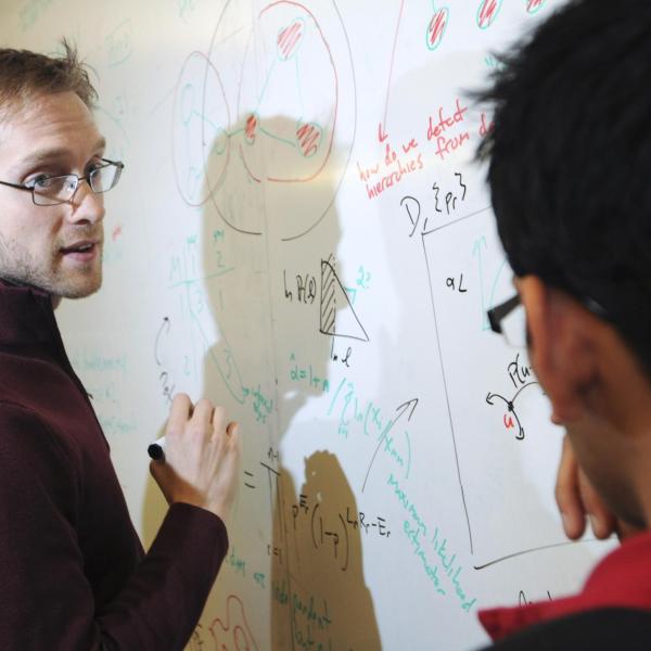 Aaron Clauset and lab member work together at a whiteboard