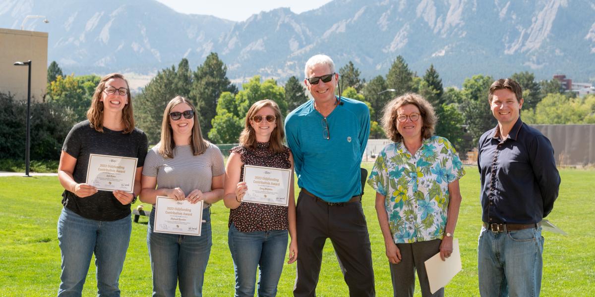 6 people standing on green grass with mountains in the background