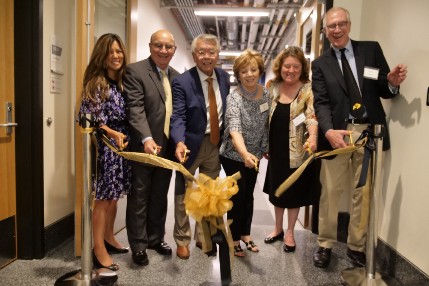 A group of people cutting a yellow ribbon in a hallway