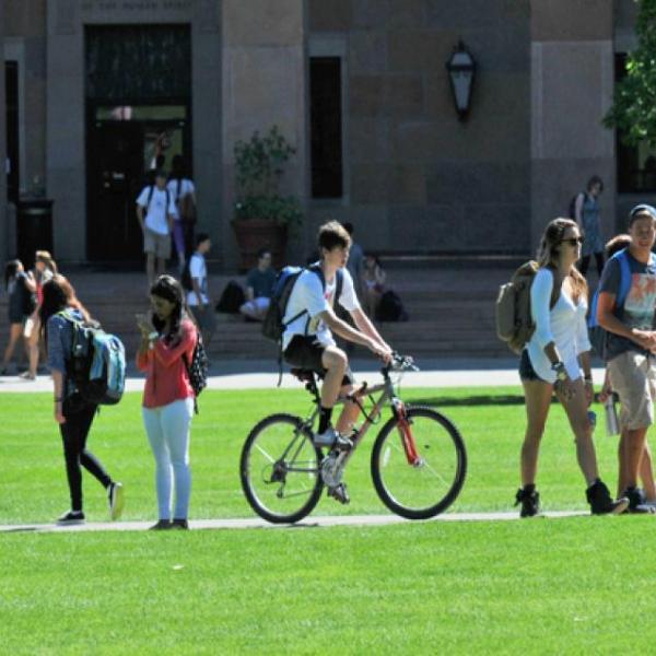 Lots of students crossing the green university lawn some on bikes and some walking 