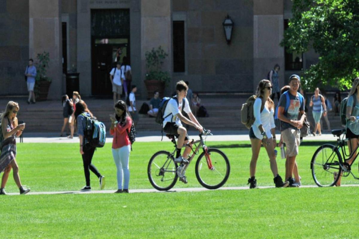 Lots of students crossing the green university lawn some on bikes and some walking