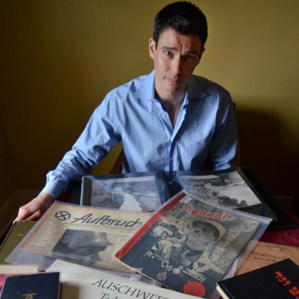 David Shneer poses with Holocaust documents. Use natural lighting and depth with wide-angle lenses to emphasize objects in the foreground.