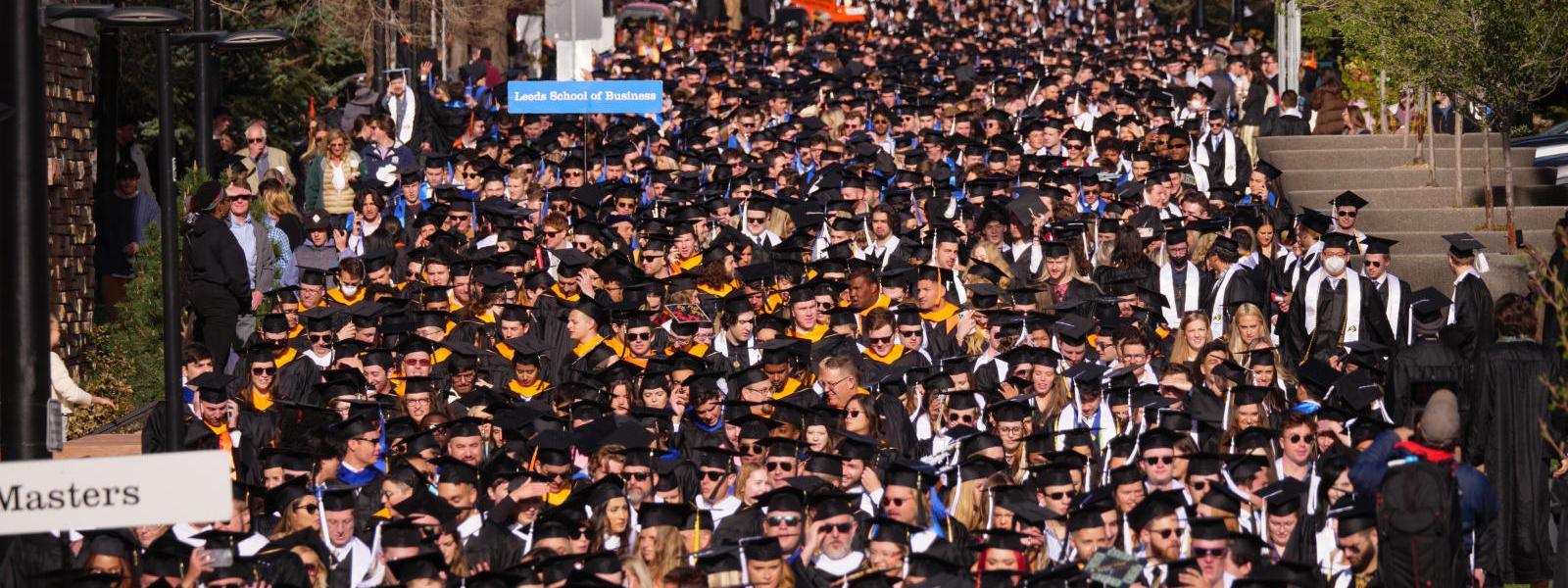 Crowd of students in regalia walking to commencement ceremony.