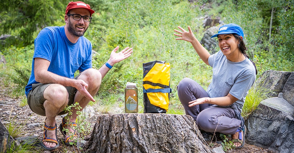 A man and a woman pose outdoors with a packraft.