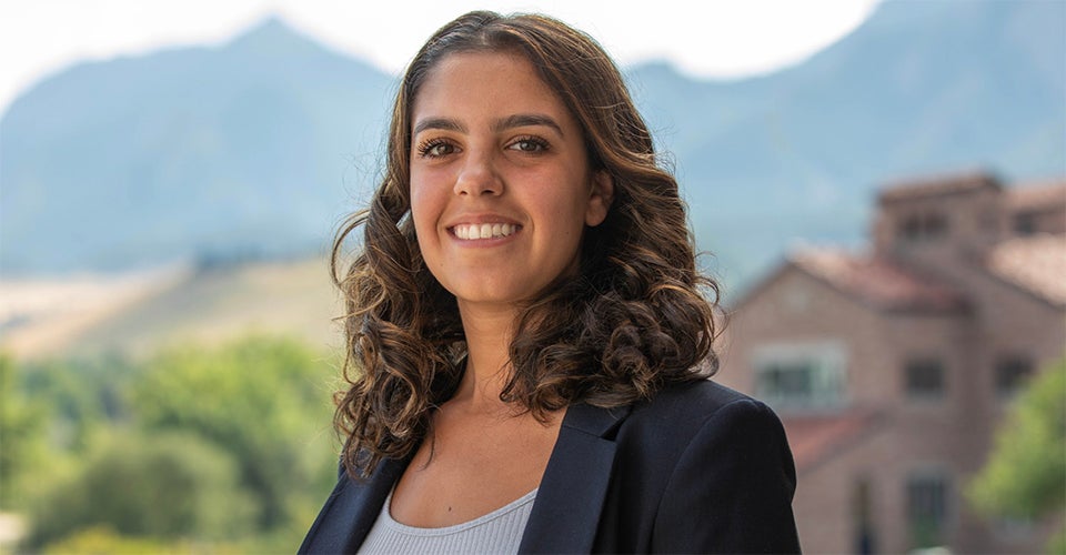 Anya Aidun in professional attire. She's standing on a balcony with the Flatirons visible in the background.