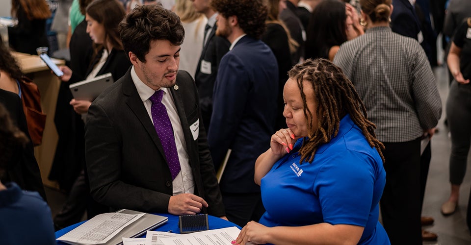 A male student and female recruiter review a resume together at a networking event in the Rustandy Building.