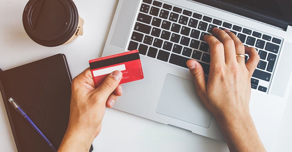 A woman pays her credit card balance using a laptop. The card is visible in the foreground.