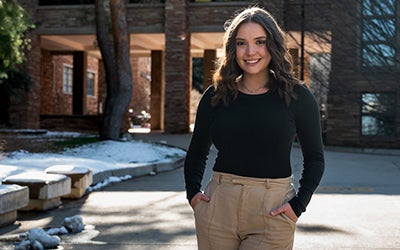 Chloe poses in casual dress on campus. A building is visible in the background.