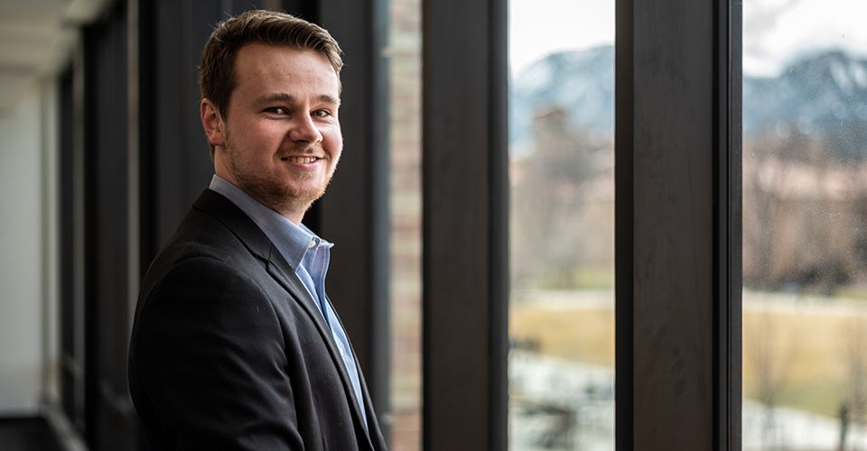 Colton in professional attire at the window of the Rustandy Building, overlooking the mountains.