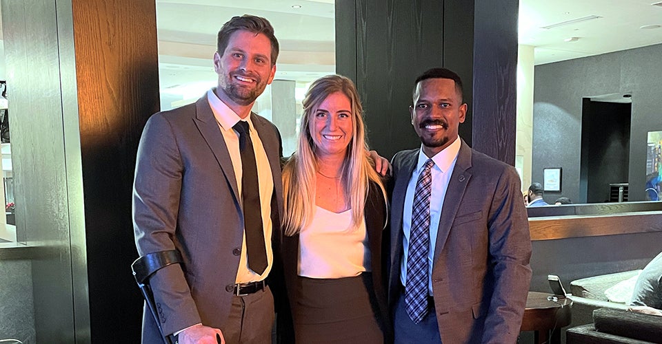 The three students on the winning team pose in a hotel lobby in business attire.